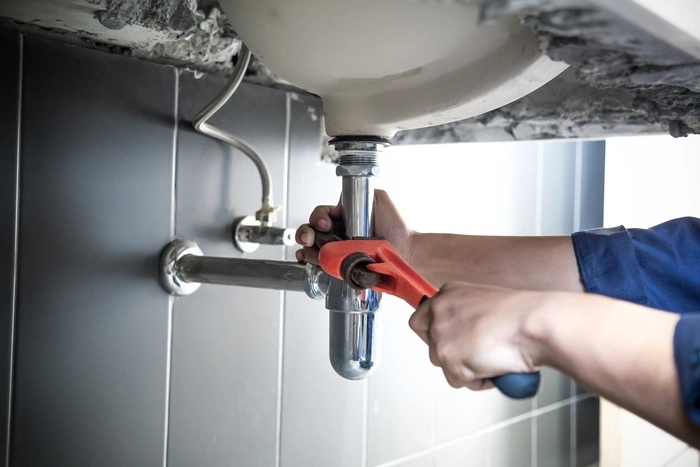 Plumber uses wrench to repair water pipe under sink There is maintenance to fix the water leak in the bathroom.with red wrench, plumbing install concept.