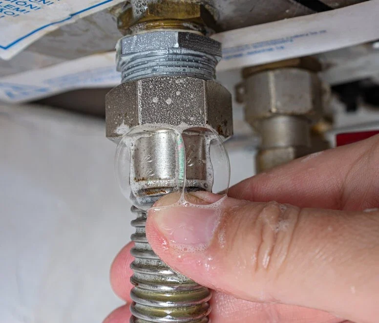 Gas leak at home boiler room. Inflating bubbles of soap mixture applied to the threaded joint on the gas flexible pipe indicate a gas leak.